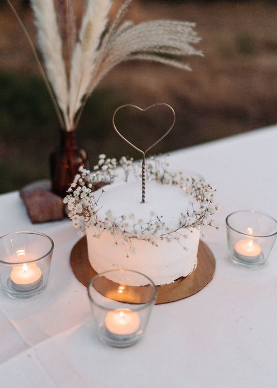 a simple white textured wedding cake with baby's breath and a wire heart topper is a cool idea for many weddings