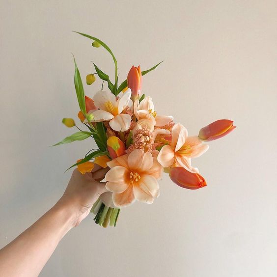 a small and gorgeous wedding bouquet made of orange and peachy tulips and greenery is cool for a bright wedding