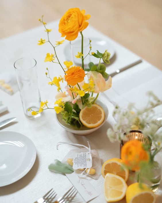 a small bold wedding centerpiece of uellow ranunculus, greenery and blooming branches plus a piece of citrus