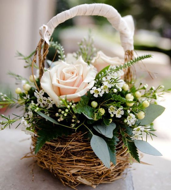 a small rustic spring wedding centerpiece of a basket with blush roses, fillers, berries and greenery is amazing