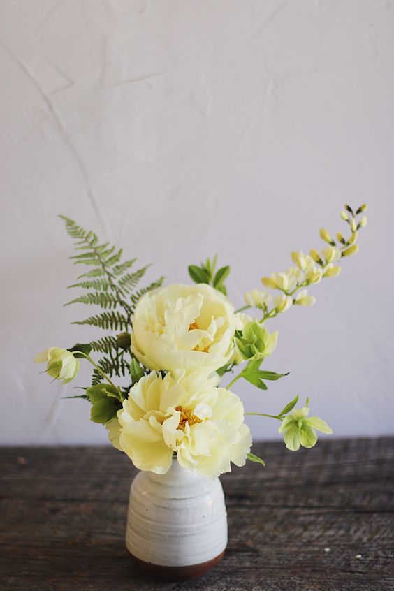 a small spring wedding centerpiece of a white vase, yellow blooms, greenery and fern is a cool idea for a bright wedding