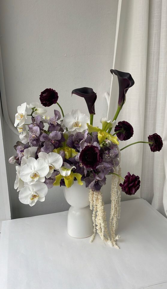 a sophisticated wedding centerpiece of deep purple ranunculus, callas, white orchids and amaranthus is wow