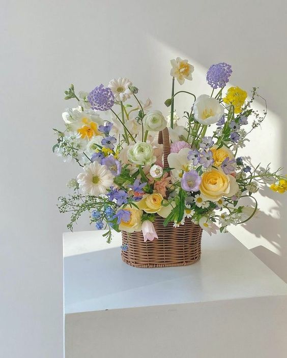 a spring basket wedding centerpiece of yellow, lilac, white and blush blooms and greenery is adorable