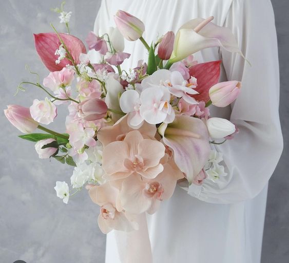 a spring wedding bouquet of white and pink tulips, blush and white orchids, sweet peas and some fillers is adorable