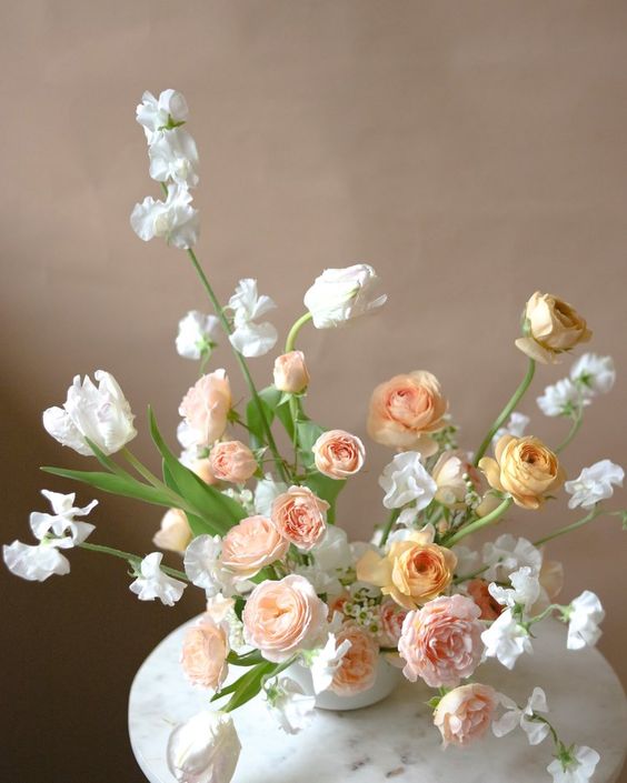 a stylish wedding centerpiece of white sweeta peas and tulips, yellow and blush ranunculus and greenery