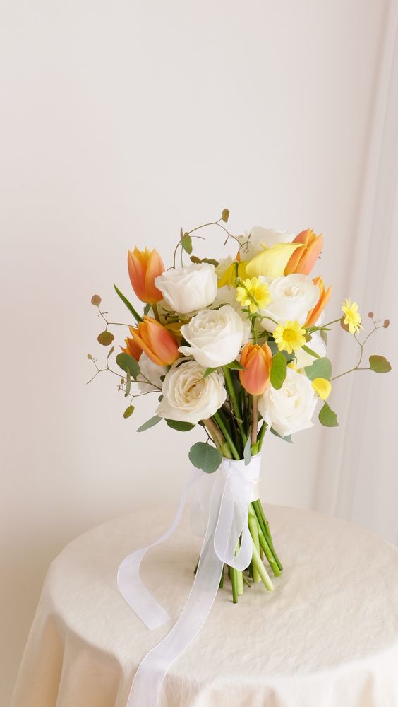 a summer wedding bouquet of white roses, orange tulips, greenery and small yellow blooms is amazing for the season
