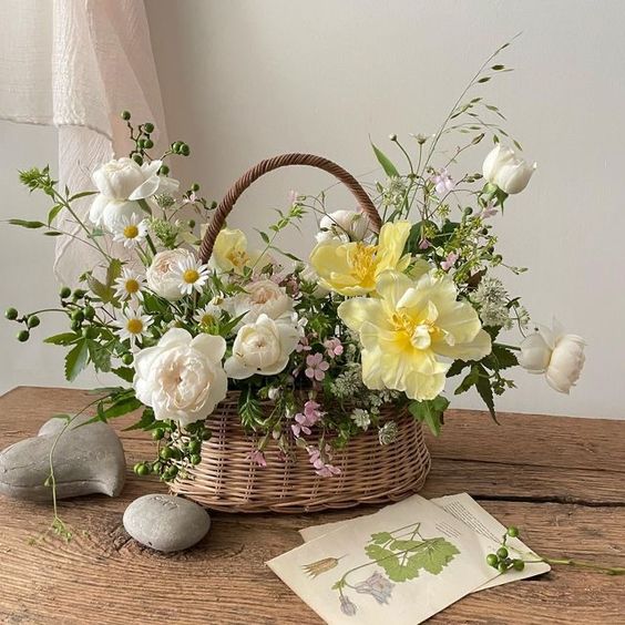 a summer wedding centerpiece in a basket, with white and yellow blooms, chamomiles and greenery is a lovely idea