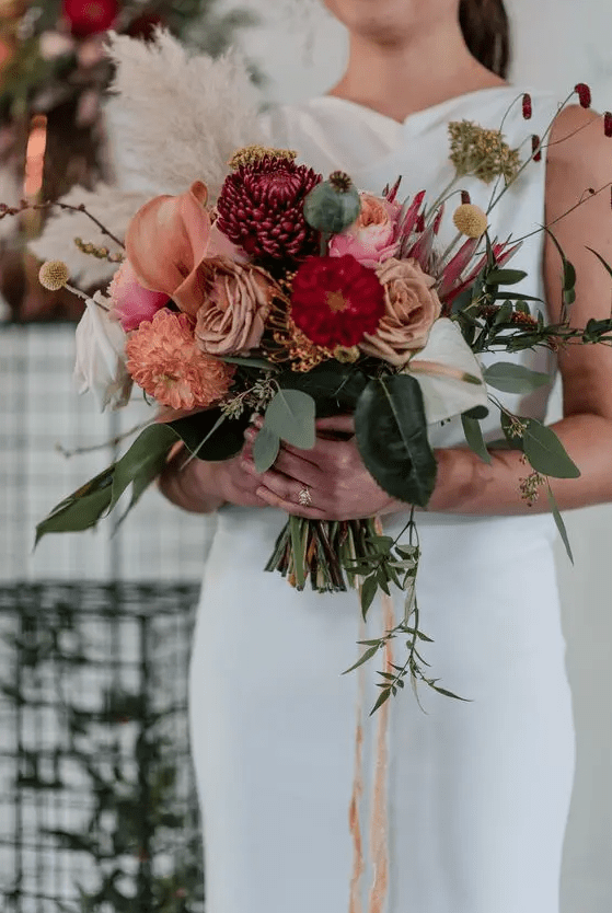A sweet fall wedding bouquet of coffee colroed roses, pink callas and dahlias, fuchsia chrysanthemums, greenery, grasses and ribbons