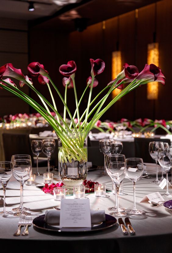 a tall modern wedding centerpiece of a clear vase with deep purple callas is a creative solution for a formal wedding