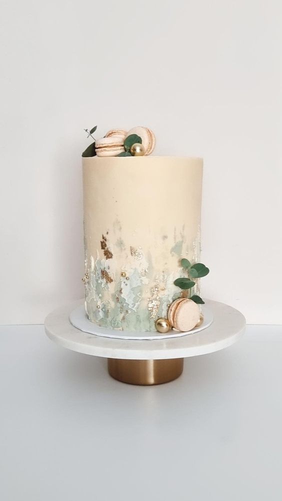 a tall tan wedding cake with green sugar details and gold, tan macarons, beads and greenery is cool for spring