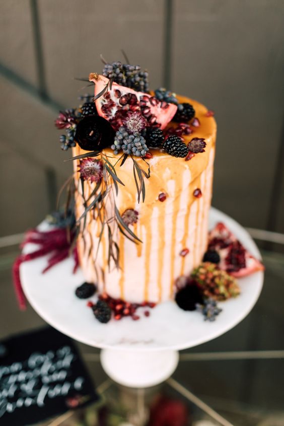 a tall wedding cake with caramel, blackberries and privet berries, deep purple blooms and pomegranate