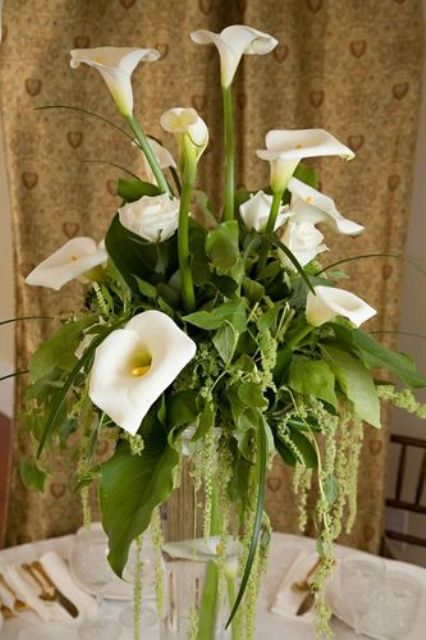 a tall wedding centerpiece of white callas, roses and greenery plus green amaranthus is trendy and cool