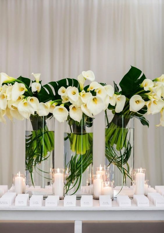 a trio of tropical wedding centerpieces of monstera leaves and white callas is perfect for a formal summer or tropical wedding