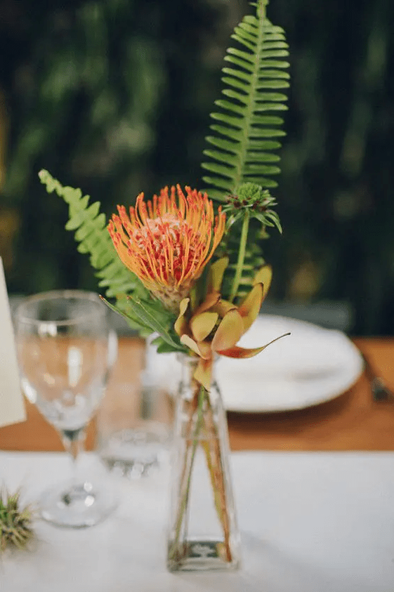 a tropical wedding centerpiece of a couple of tropical blooms and fern is a lovely and cool idea for a modern wedding
