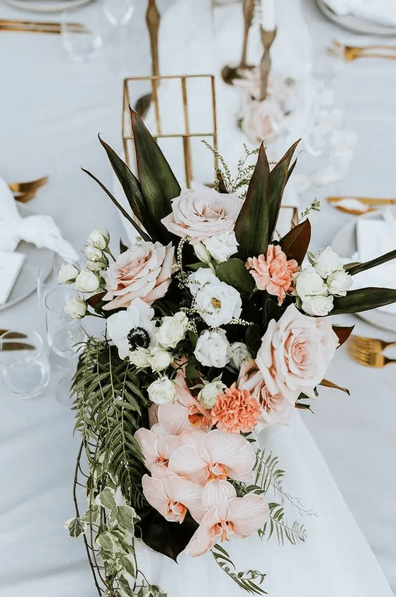 A tropical wedding centerpiece of roses, anemones, orchids and greenery and leaves is a very eye catchy decoration for  a modern wedding