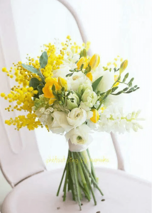 a virbant wedding bouquet of white and yellow tulips and freesia, yellow mimosa and greenery for a spring wedding