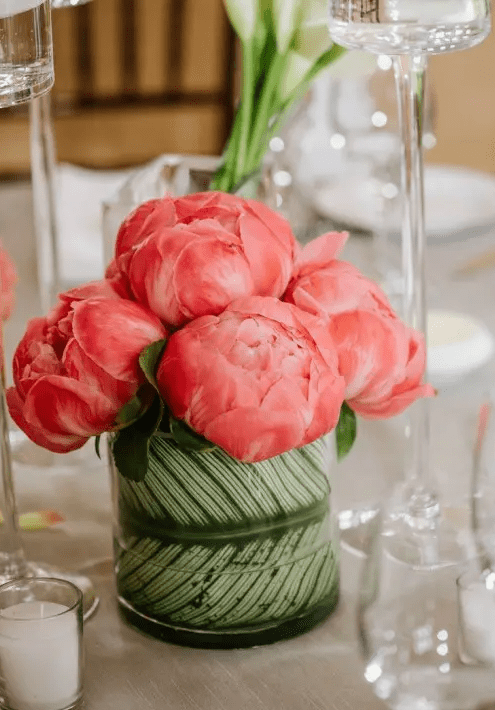 a vivacious summer wedding centerpiece of coral peonies and a vase wrapped with a large leaf is a stylish and inspiring summer wedding centerpiece