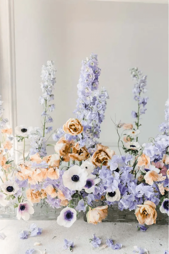 a wedding centerpiece made of white anemones, purple ranunculus and orange tulips is a unique and colorful combo for a wedding