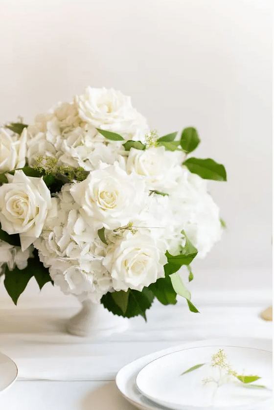 a white hydrangea and rose wedding centerpiece with leaves is a stylish idea for a chic and classic wedding