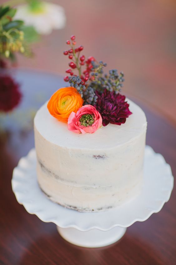 a white naked wedding cake topped with fresh blooms and berries is a bold solution for the fall