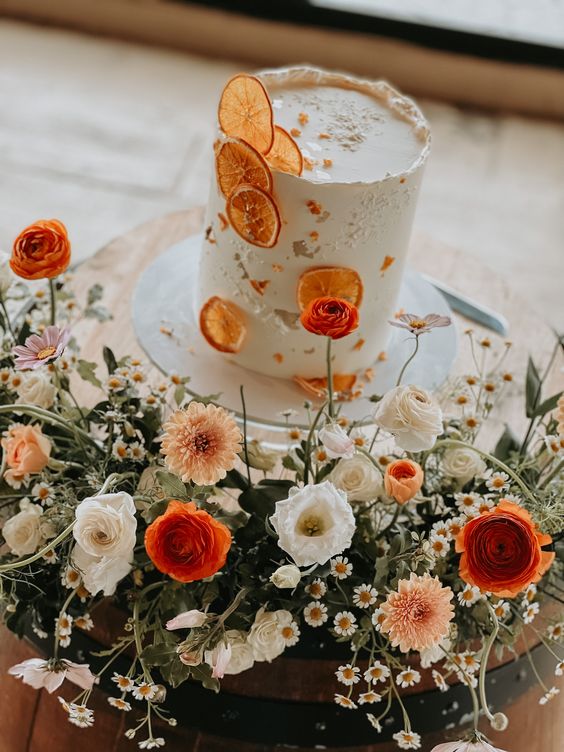 a white textural wedding cake with dried citrus and orange and white blooms around the cake is cool for the fall