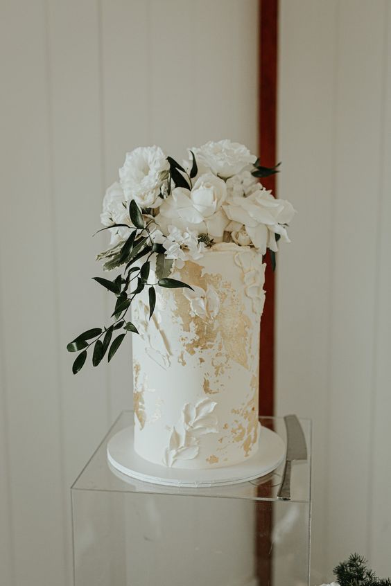 a white textural wedding cake with gold leaf and white blooms and greenery on top is a timeless and cool idea