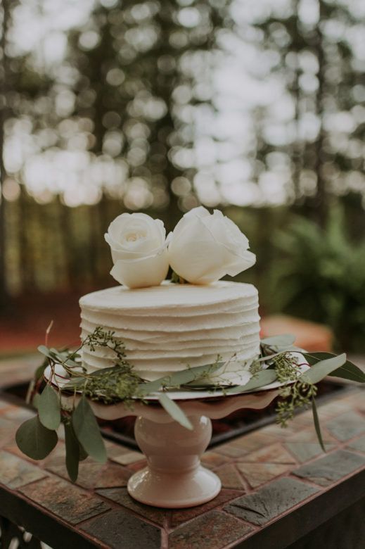 a white textured wedding cake decorated with greenery and white roses is a lovely idea for any small wedding, it will fit anything