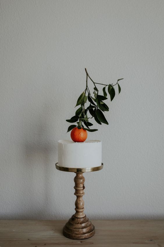 a white textured wedding cake topped with a single orange with leaves is a super cool idea for summer