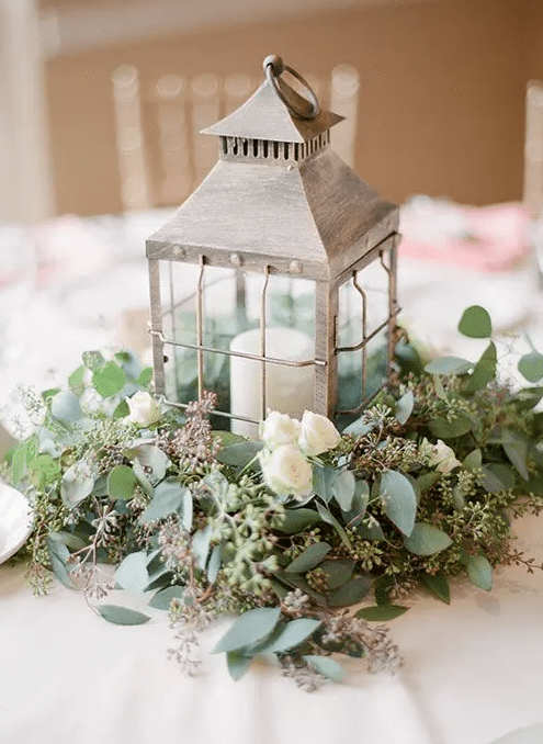 a whitewashed candle lantern on a eucalyptus and white roses pad for a vintage or garden wedding tablescape
