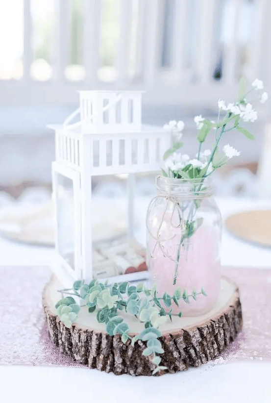 a wood slice, a white candle lantern with wine corks, a pink jar with some wildflowers and eucalyptus