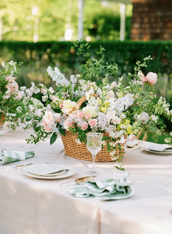 an amazing garden wedding centerpiece of a basket with greenery, yellow, pink and blue flowers looks very natural and pretty