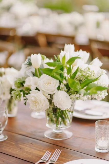 an ethereal wedding centerpiece of a clear vase with greenery, white tulips and roses is always a good idea
