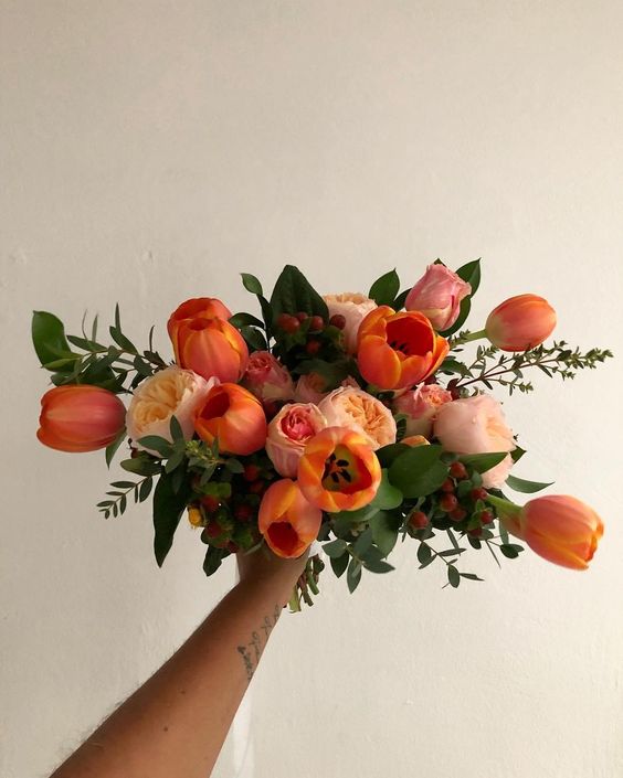 an extra bold spring wedding bouquet of orange tulips and blush peony roses plus berries and leaves can be rocked in the fall, too