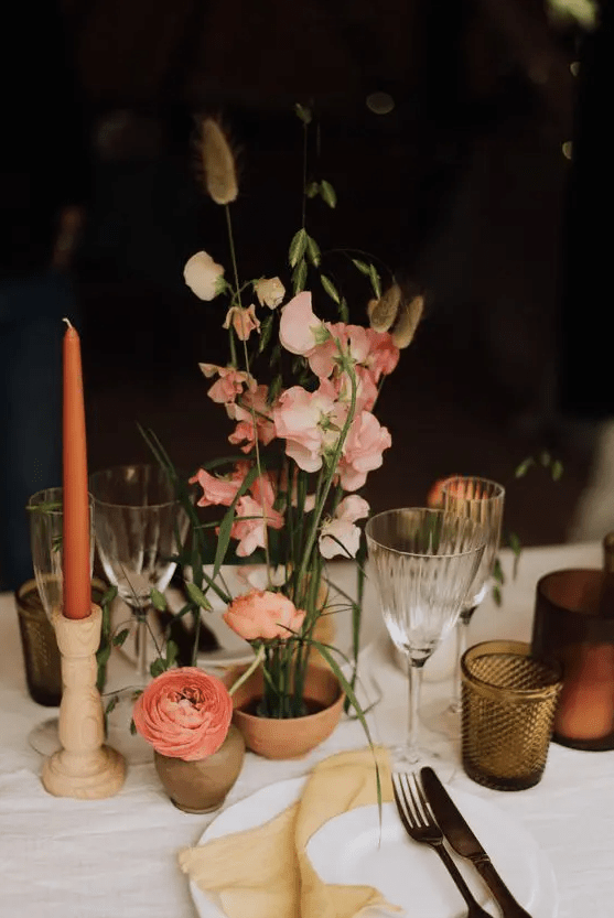 an ultra-modern wedding centerpiece of pink and peachy sweet peas and bunny tails ina terracotta pot and some pink ranunculus