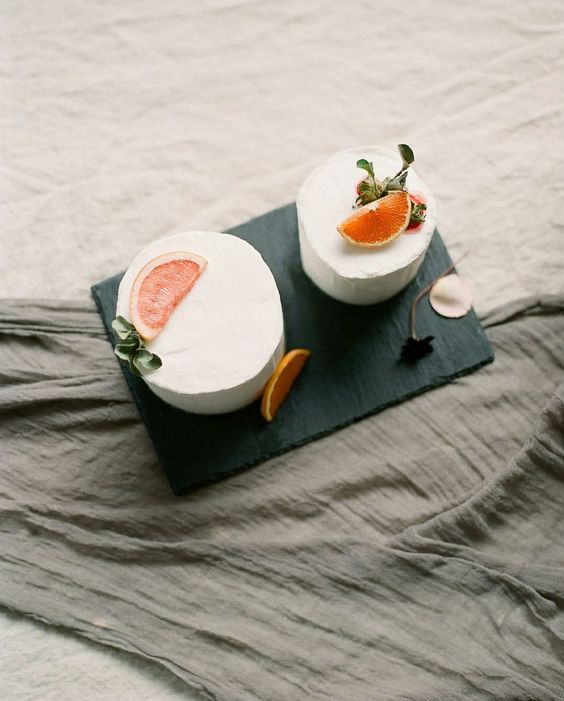 two sleek white wedding cakes topped with a bit of leaves and fruit slices are amazing for a refined wedding