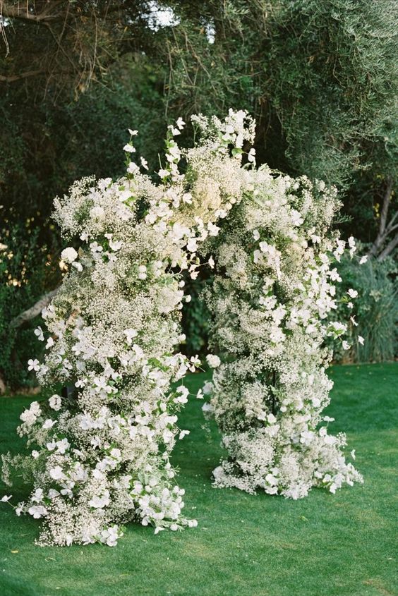a super lush white wedding arch done with baby's breath and many other blooms is a cool idea for spring and summer