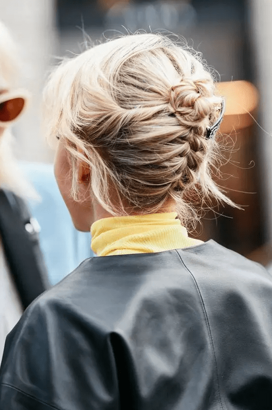A backward braided updo with a tiny bun on top and some face framing hair for a cool look