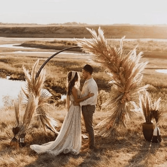 a boho fall round wedding arch with pampas grass, bold dried blooms and leaves plus pampas grass in vases around