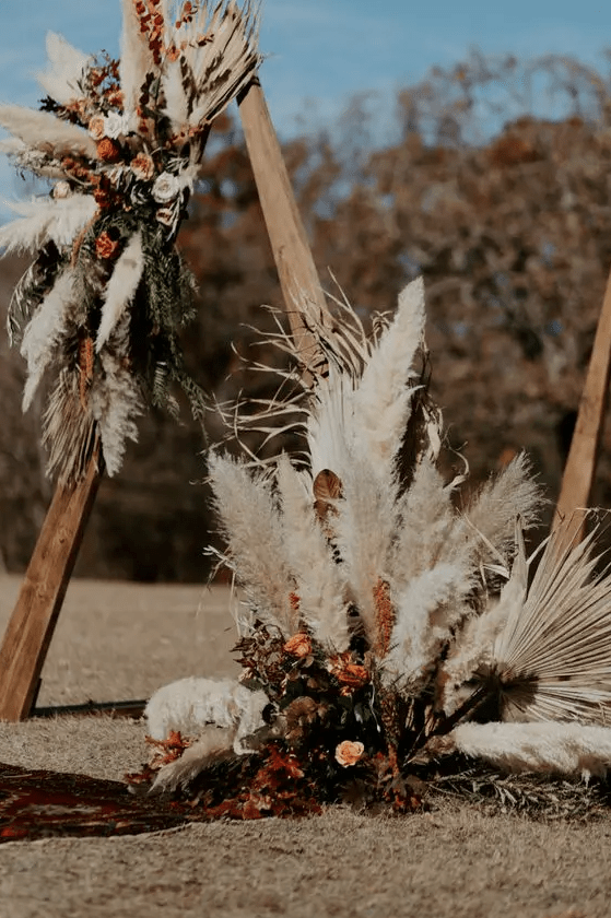 a boho fall triangle wedding arch with pampas grass, dried leaves, blush, rust and burgundy blooms is amazing