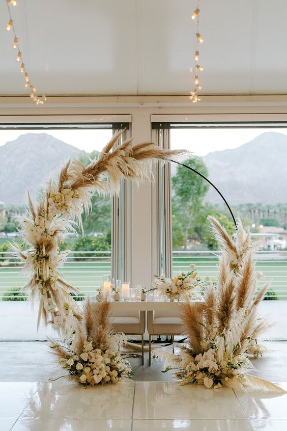 a boho round wedding arch covered with pampas grass and neutral blooms is a lovely idea for a spring or summer wedding