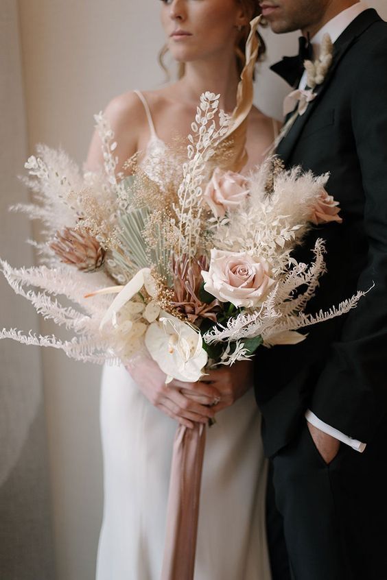 a boho wedding bouquet of blush roses, white anhturiums, king proteas, pampas grass and green fronds