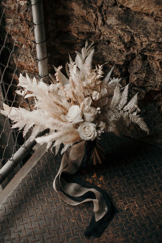a boho wedding bouquet of white roses, dried leaves and grasses is a cool idea for a neutral boho wedding