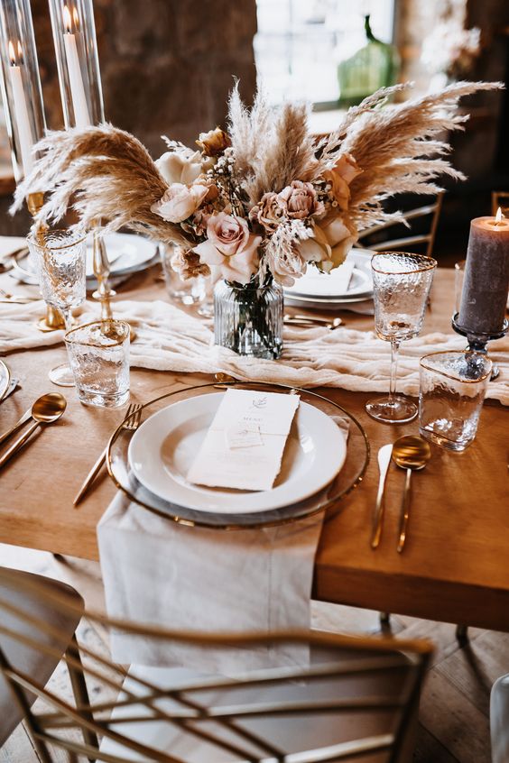 a boho wedding centerpiece of pampas grass, blush roses and some fillers is a romantic and elegant idea for a neutral-colored wedding