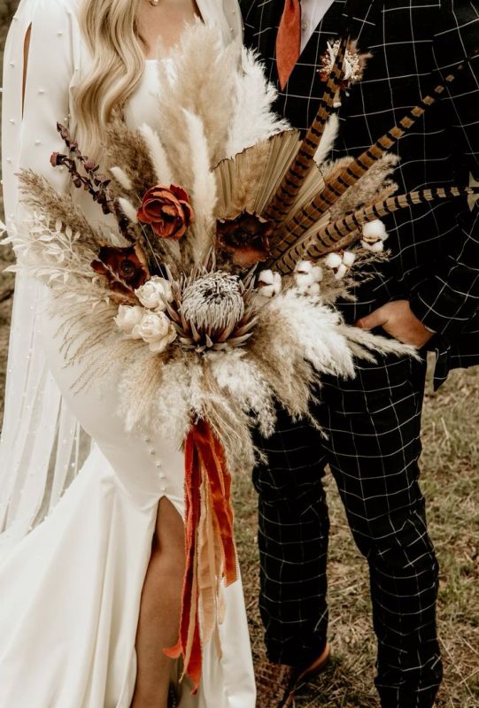 a bold fall wedding bouquet of pampas grass, fronds, feathers, dried grasses and flowers is a cool idea for a boho wedding