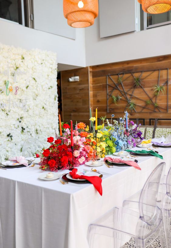 a bold gradient wedding centerpiece from red to pink, yellow, green, blue and purple, with roses and baby’s breath and colorful candles