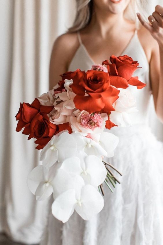 a bold modern wedding bouquet of large blush and red roses and white orchids is amazing