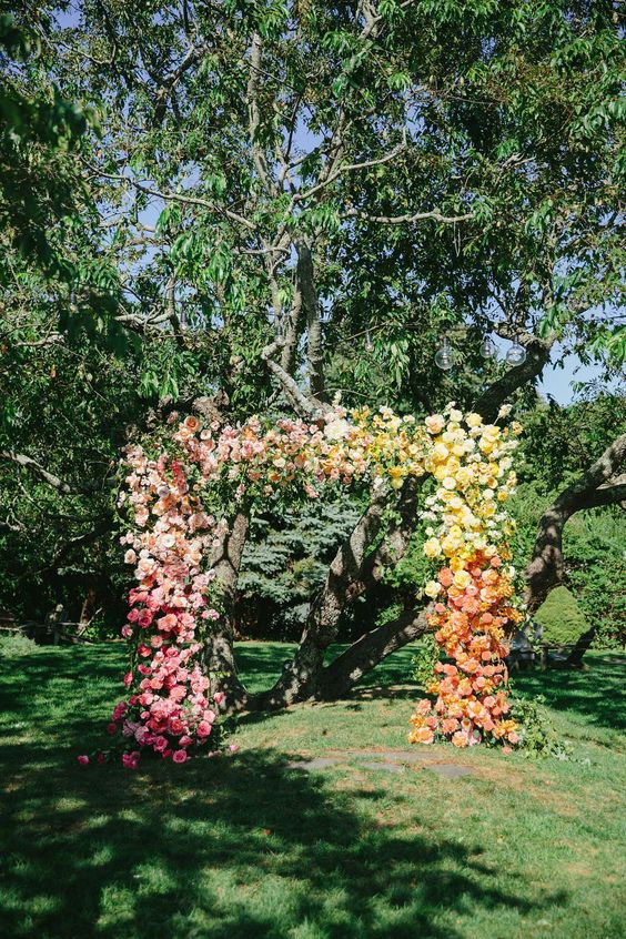 a bold ombre wedding arch from pink to yellow and orange is a stunning idea for a colorful summer wedding
