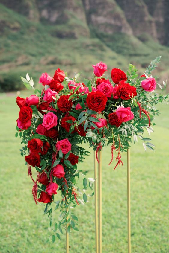 a bold tall wedding centerpiece of pink and red roses and peonies and greenery is adorable for a colorful wedding