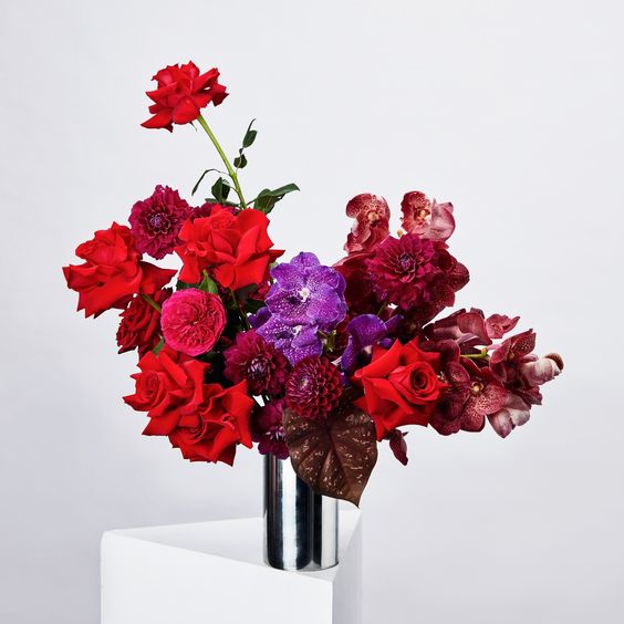 a bold wedding centerpiece of burgundy, red  roses, violet blooms and some dark foliage for a Halloween wedding