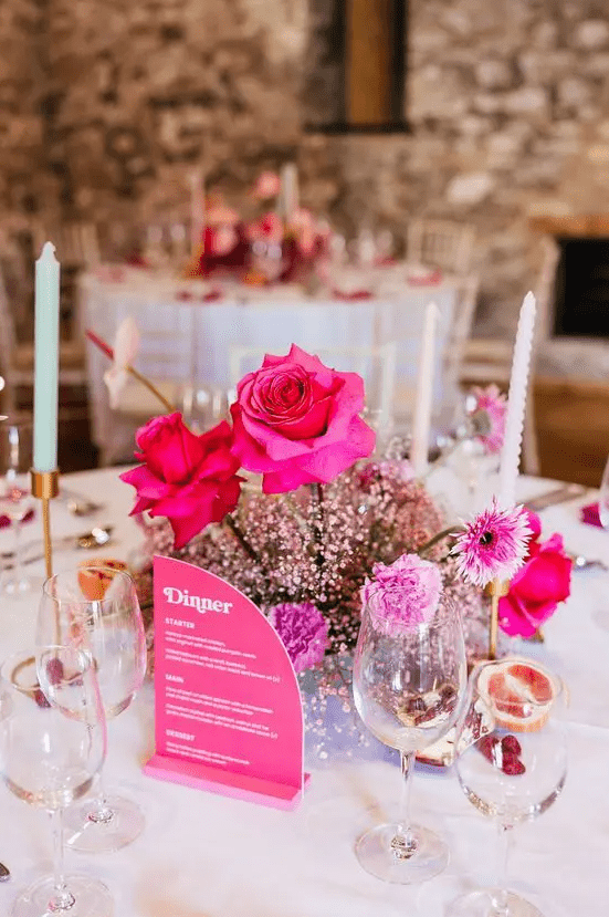 a bold wedding centerpiece of pink baby's breath, hot pink roses and carnations and a pink menu next to it is a cool idea